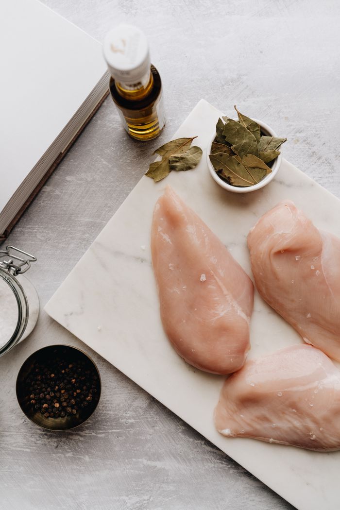 Top view of raw chicken breasts with herbs and olive oil on a marble board in the kitchen.